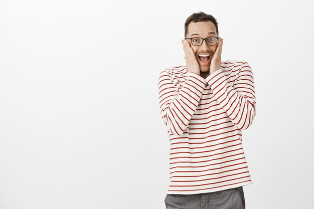 Retrato de alegre chico guapo sobre-emotivo con gafas, gritando de placer y sorpresa