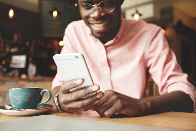 Retrato de alegre estudiante afroamericano escribiendo un mensaje en el teléfono inteligente