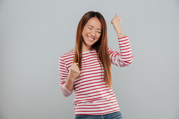 Retrato de una alegre muchacha asiática celebrando el éxito mientras está de pie