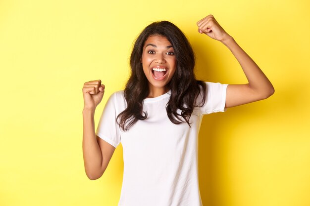 Retrato de alegre niña afroamericana ganando y celebrando la victoria levantando las manos