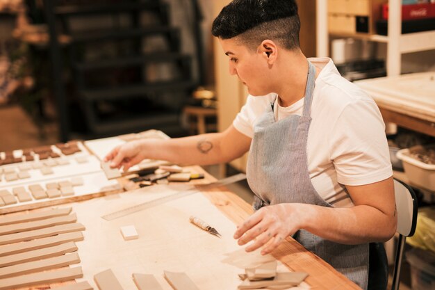 Retrato de un alfarero que arregla los azulejos de arcilla en la mesa de madera en el taller