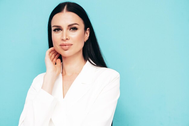 Retrato de alta moda de joven hermosa mujer morena con bonito traje blanco de moda Modelo de moda sexy posando en el estudio Mujer de moda aislada en azul