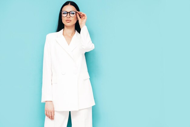 Retrato de alta moda de joven hermosa mujer morena con bonito traje blanco de moda Modelo de moda sexy posando en el estudio Mujer de moda aislada en azul