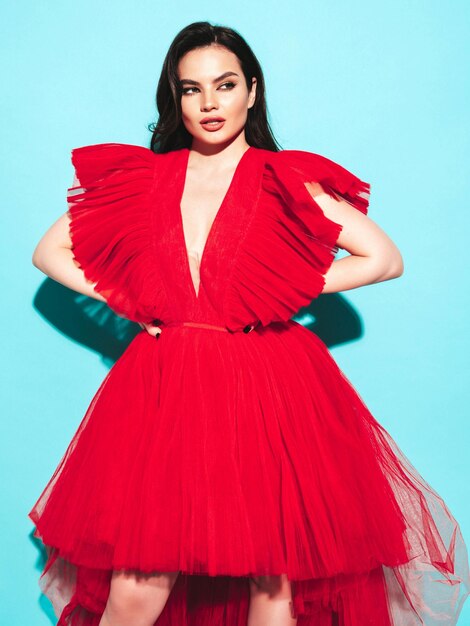 Retrato de alta moda de joven hermosa mujer morena con un bonito vestido rojo de noche esponjoso Modelo de moda sexy posando en el estudio Mujer de moda aislada en azul