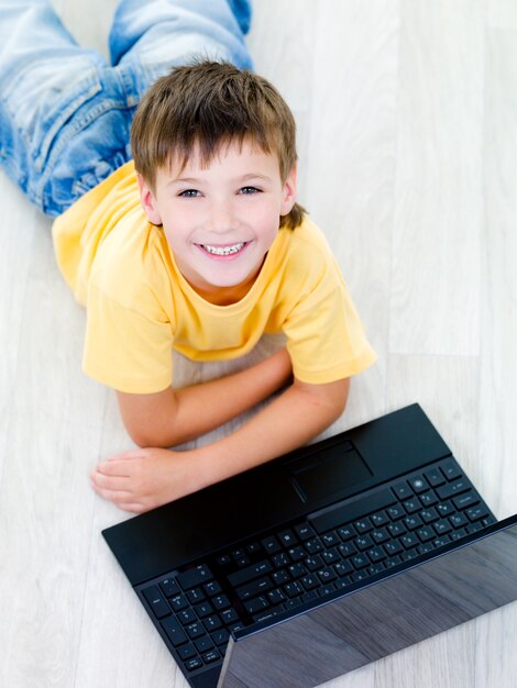Retrato de alto ángulo de niño alegre feliz con portátil en el suelo