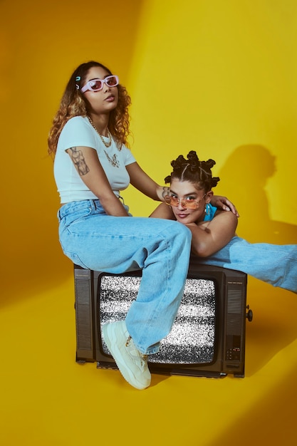 Retrato de amigas en el estilo de moda de la década de 2000 posando junto con la televisión