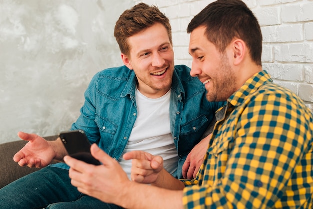 Foto gratuita retrato de un amigo masculino sonriente que muestra algo en el teléfono inteligente a su amigo