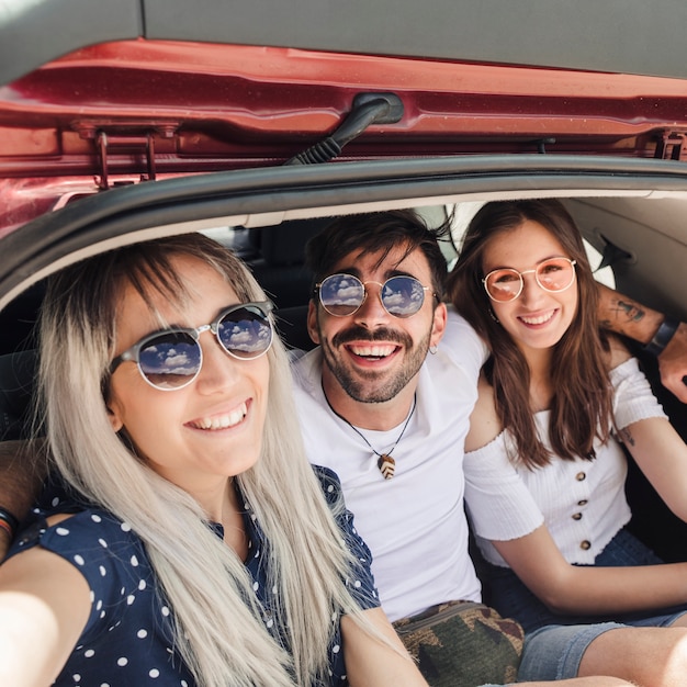 Retrato de amigos felices que se sientan dentro del tronco del coche