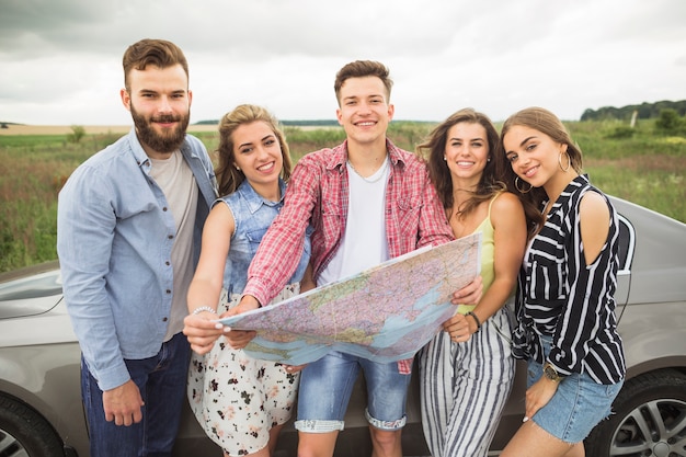 Retrato de amigos con mapa turístico de pie junto al coche