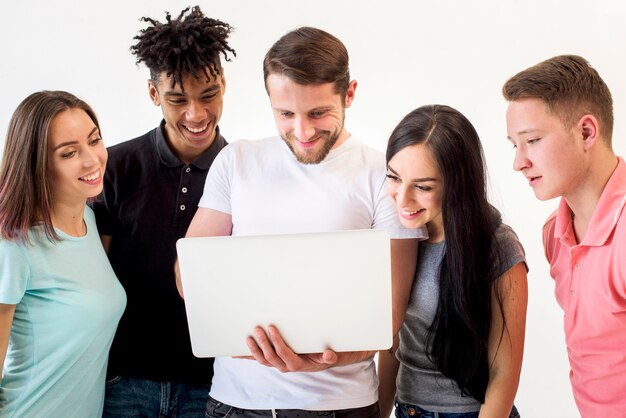 Retrato de los amigos multiétnicos que miran en la computadora portátil que se coloca en el fondo blanco