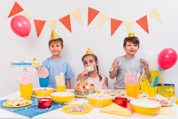 Retrato de los amigos sonrientes que sostienen la tarjeta sonriente; Globo y confeti con comida en mesa.