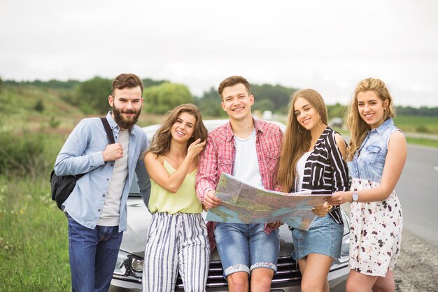 Retrato de amigos de turistas con mapa de pie delante del coche al aire libre