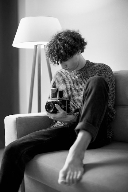 Retrato analógico en blanco y negro de un hombre guapo posando en el interior del sofá con cámara