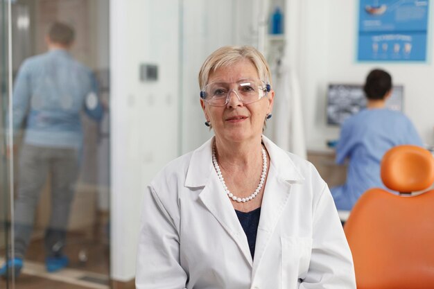 Retrato de una anciana dentista que trabaja en la oficina del hospital estomatológico esperando que el paciente enfermo comience el examen dental. Equipo médico que trabaja en el tratamiento de la salud. Servicios de medicina