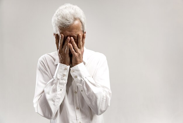 Retrato de anciano molesto que cubre la cara mientras llora. Aislado en la pared gris