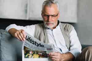 Foto gratuita retrato de un anciano sentado en el sofá leyendo el periódico