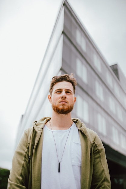 Foto gratuita retrato de ángulo bajo de un hombre joven con una camiseta gris con una chaqueta y posando al aire libre