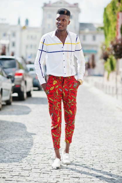 Retrato de un apuesto y elegante modelo afroamericano con pantalones rojos y camisa blanca posando en la calle