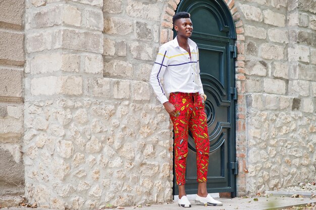 Retrato de un apuesto y elegante modelo afroamericano con pantalones rojos y camisa blanca