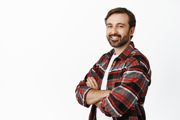 Retrato de un apuesto hombre adulto seguro de sí mismo con los brazos cruzados de la barba en el pecho que parece un profesional de pie sobre un fondo blanco