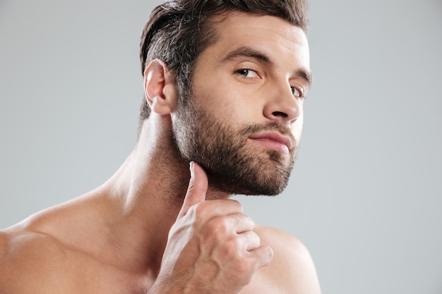 Retrato de un apuesto hombre barbudo desnudo examinando su rostro