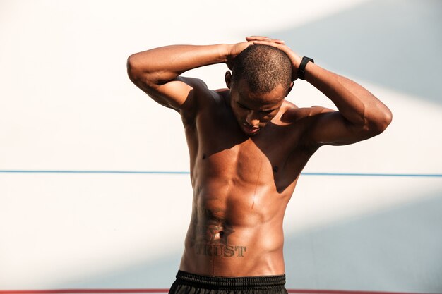 Retrato de un apuesto hombre deportivo africano con las manos detrás de la cabeza, descansando después del entrenamiento