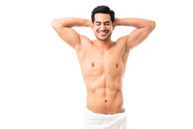 Retrato de un apuesto hombre musculoso de pie con las manos detrás de la cabeza y sonriendo sobre fondo blanco.