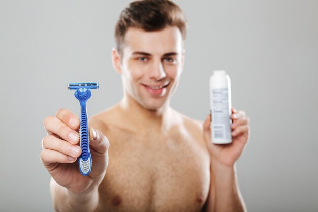 Retrato de un apuesto hombre semidesnudo mostrando maquinilla de afeitar