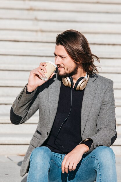 Retrato de un apuesto joven con auriculares alrededor de su cuello tomando café para llevar