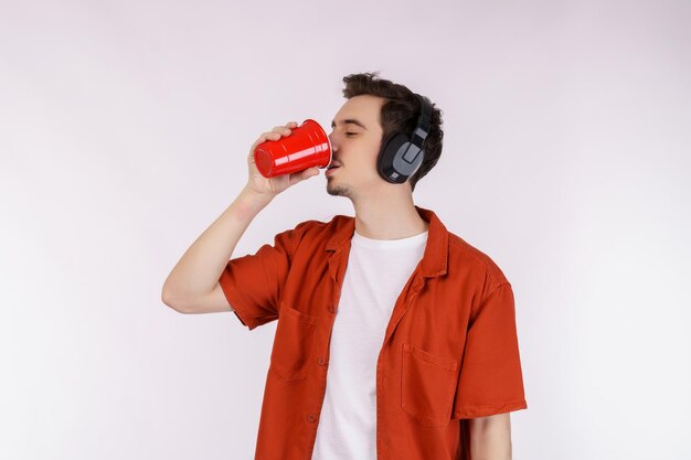 Retrato de un apuesto joven con auriculares de pie y bebiendo café aislado fondo blanco.