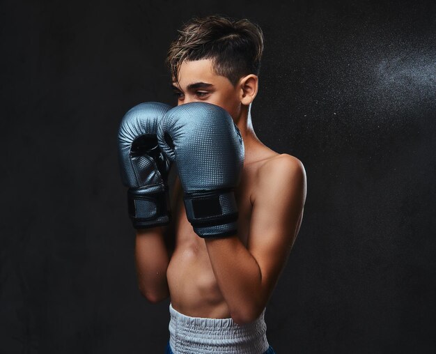 Retrato de un apuesto joven boxeador sin camisa con guantes. Aislado en el fondo oscuro.