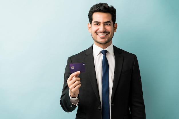 Retrato de un apuesto joven hombre de negocios que muestra su tarjeta de crédito mientras se enfrenta a un fondo aislado