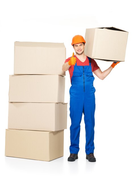 Retrato de apuesto joven repartidor con cajas de papel mostrando el pulgar hacia arriba signo aislado en blanco