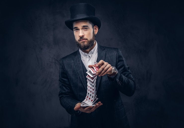 Foto gratuito retrato de un apuesto mago con traje negro, mostrando trucos con cartas en un fondo oscuro.