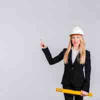 Foto gratuita retrato de un arquitecto femenino joven que lleva el casco de protección que señala su dedo contra fondo gris