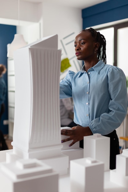 Retrato de arquitecto mirando el diseño arquitectónico de un edificio futurista en el escritorio con maqueta de proyecto residencial. Ingeniero inspeccionando el modelo de rascacielos en la oficina arquitectónica moderna.