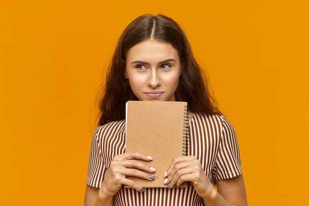 Retrato de artista joven atractiva talentosa en vestido rayado que sostiene el nuevo cuaderno de bocetos