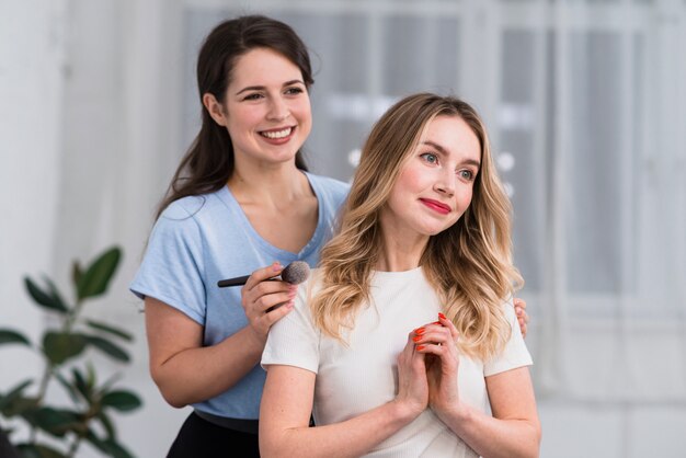 Retrato del artista de maquillaje que usa el cepillo y la mujer rubia feliz