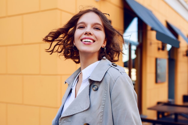 Retrato ascendente cercano positivo de la muchacha de pelo corto feliz sonriente con los dientes blancos perfectos que se divierten. Vellos ventosos. Humor de otoño