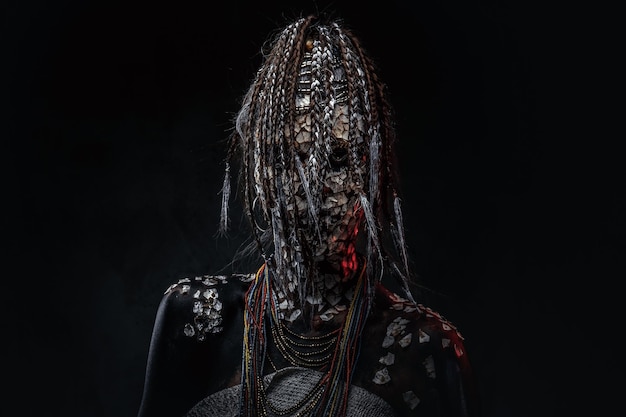 Retrato de una aterradora chamán africana con una piel agrietada petrificada y rastas en un fondo oscuro. Concepto de maquillaje.