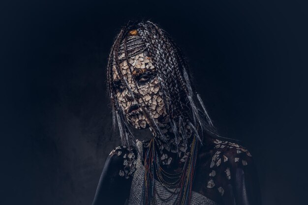 Retrato de una aterradora chamán africana con una piel agrietada petrificada y rastas en un fondo oscuro. Concepto de maquillaje.