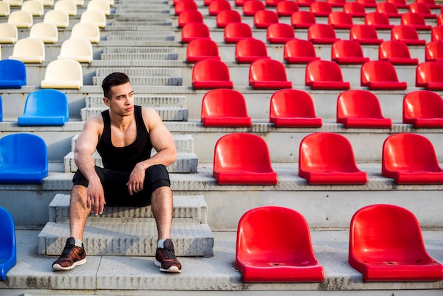 Retrato de un atleta masculino sentado en los escalones de la grada de hormigón