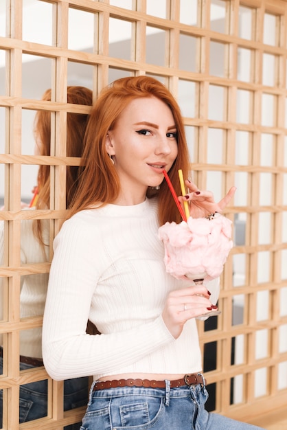 Retrato de una atractiva joven sosteniendo el vaso de coctel de verano cubierto con algodón de azúcar