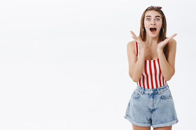 Foto gratuita retrato de atractiva mujer caucásica emotiva en la parte superior a rayas y diadema dejando caer la mandíbula de asombro y sorpresa gesticulando con las manos mirando impresionado y emocionado