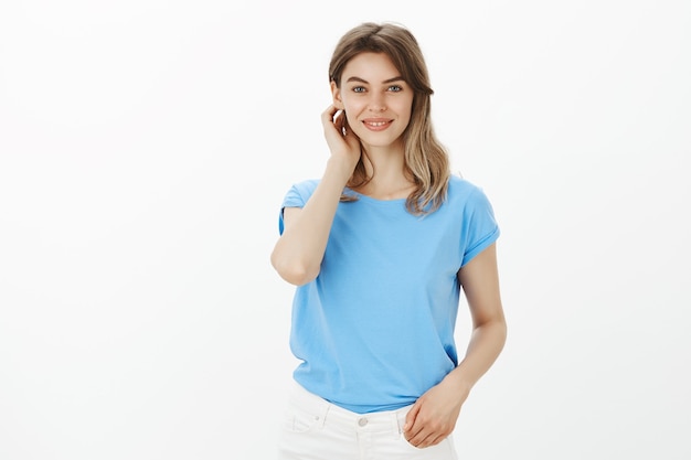 Retrato de atractiva mujer rubia modesta meter el pelo detrás de la oreja y sonriendo lindo