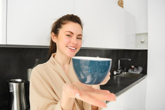 Retrato de una atractiva mujer sonriente que le da una taza ofreciendo café por la mañana y luciendo feliz