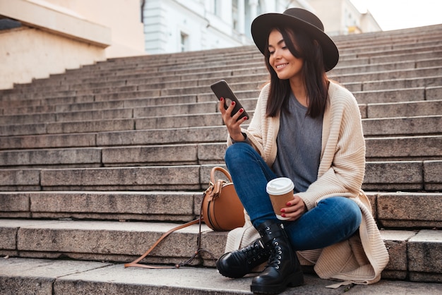 Retrato de una atractiva mujer sonriente mediante teléfono móvil