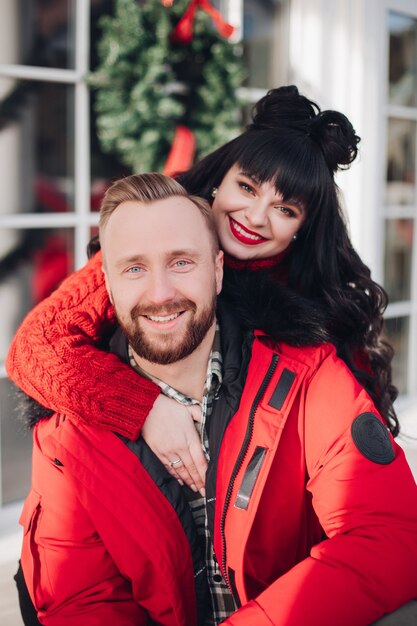 Retrato de una atractiva pareja caucásica en rojo sonriendo a la cámara. Guirnalda de Navidad borrosa en segundo plano.