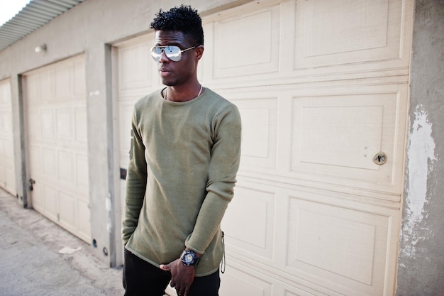 Retrato de un atractivo afroamericano negro con gafas de sol posando y de pie junto a las puertas del garaje