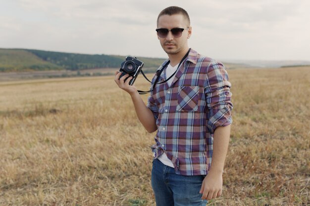 Retrato de atractivo fotógrafo masculino al aire libre al atardecer. Joven con una cámara en mano